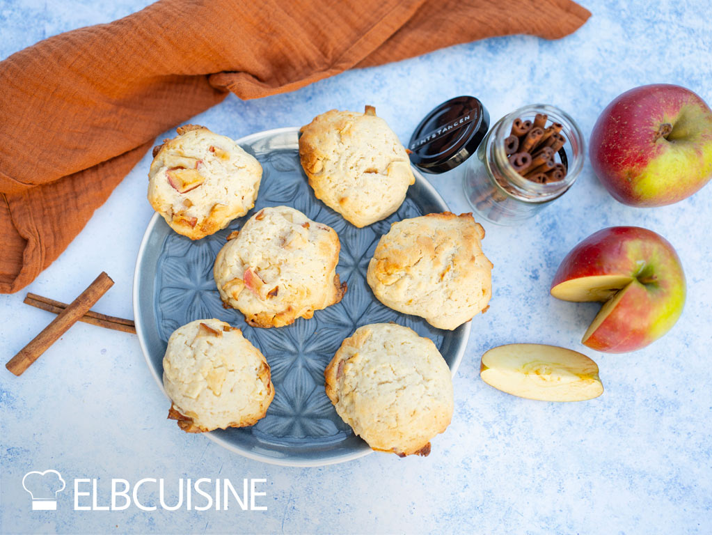 Cheesecake-Cookies liegen auf einem Teller, rechts daneben liegen Äpfel und Zimtstangen