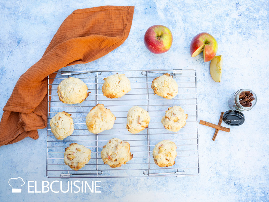 Cheesecake-Cookies liegen auf einem Ofenrost, rechts daneben liegen Äpfel und Zimtstangen