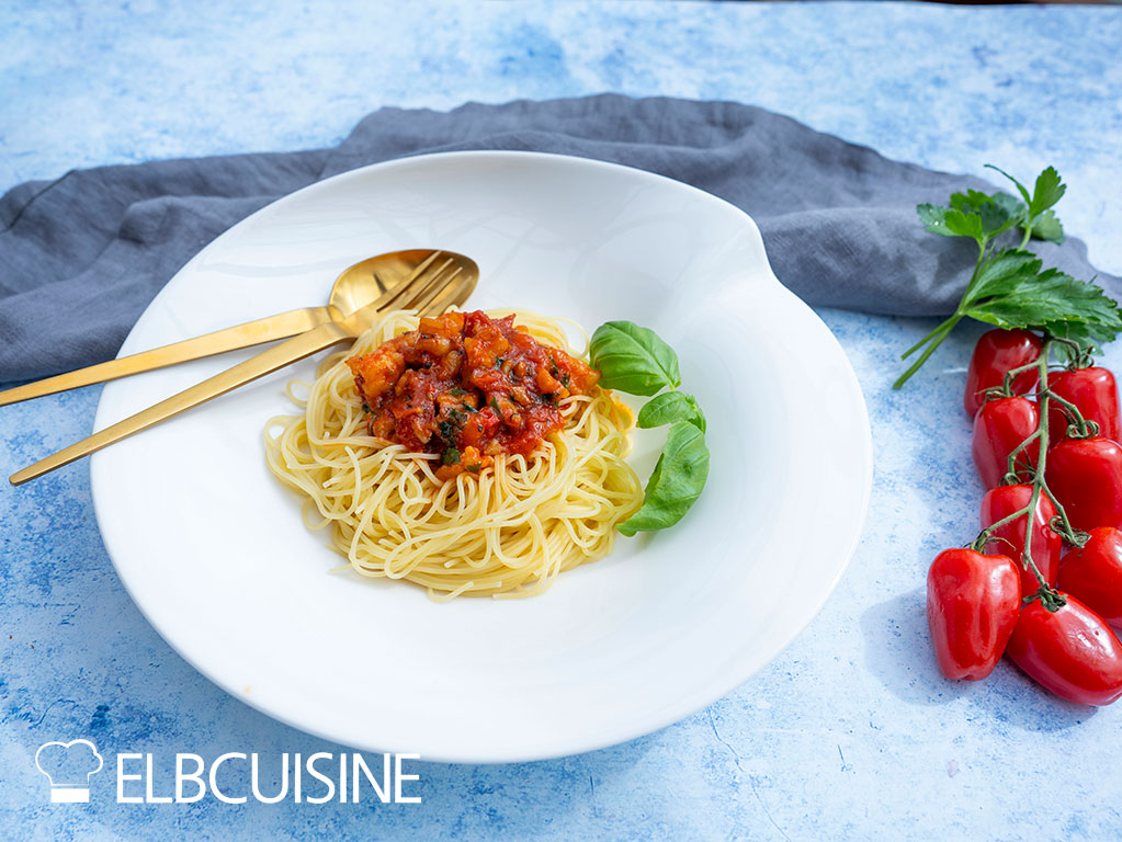 Spaghetti mit Garnelen-Bolognese auf einem Teller angerichtet. Dekoriert mit Basilikum und Tomatenrispe.