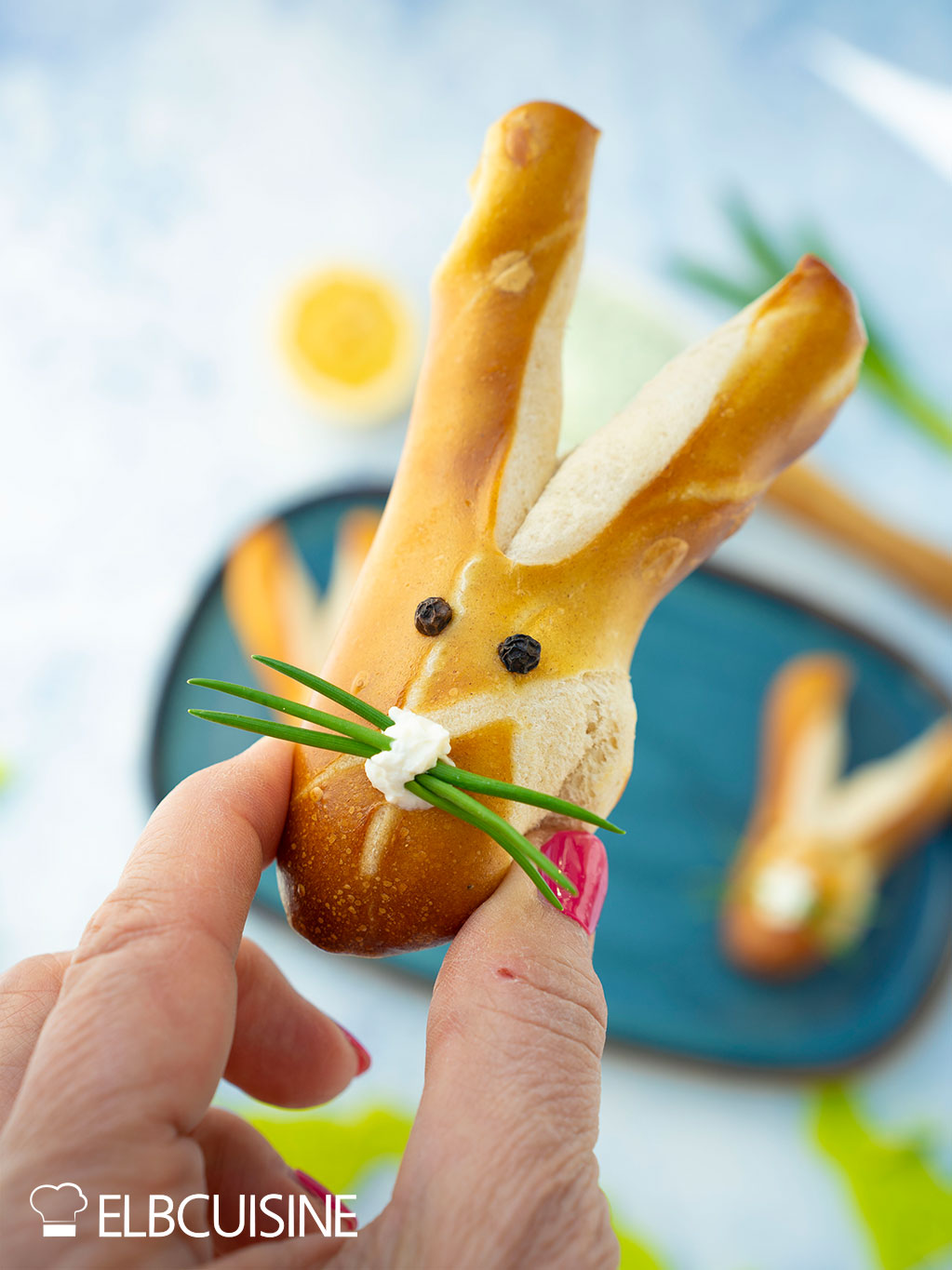 Ein goldbraun gebackenes Laugenbrötchen in niedlicher Hasenform mit langen Ohren und einer Nase aus Frischkäse und Schnurrhaare aus Schnittlauch bereit für den Osterbrunch.